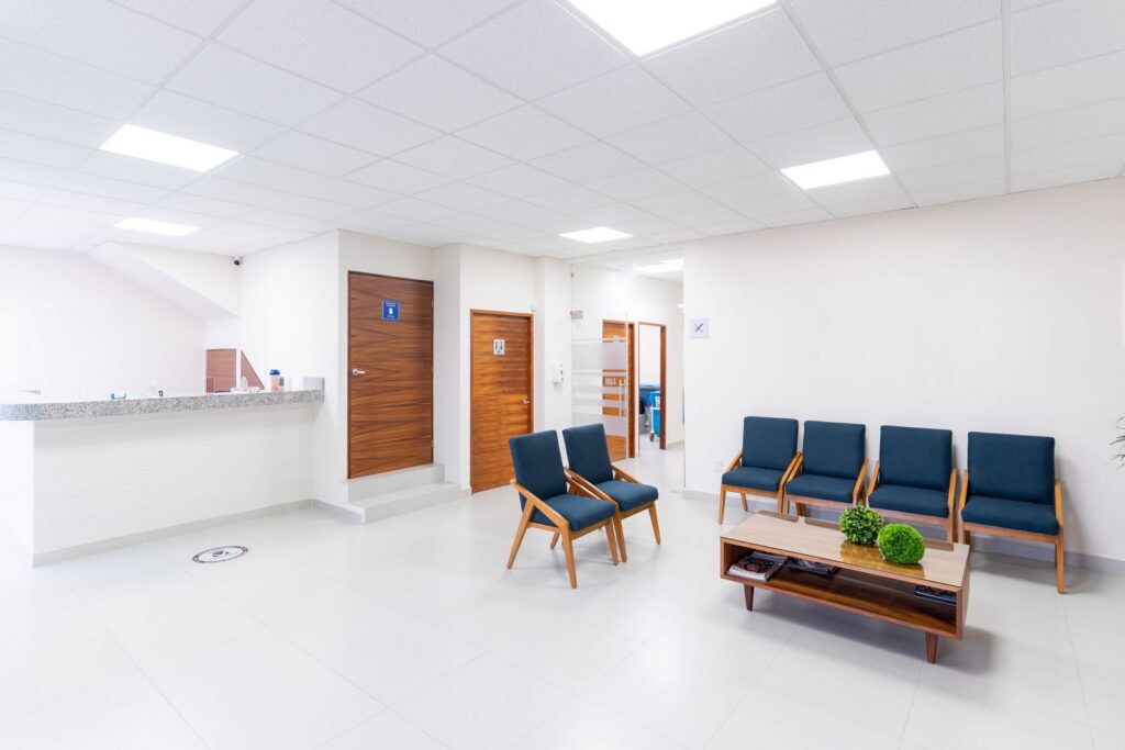 An empty medical waiting room with rows of chairs and a reception counter.